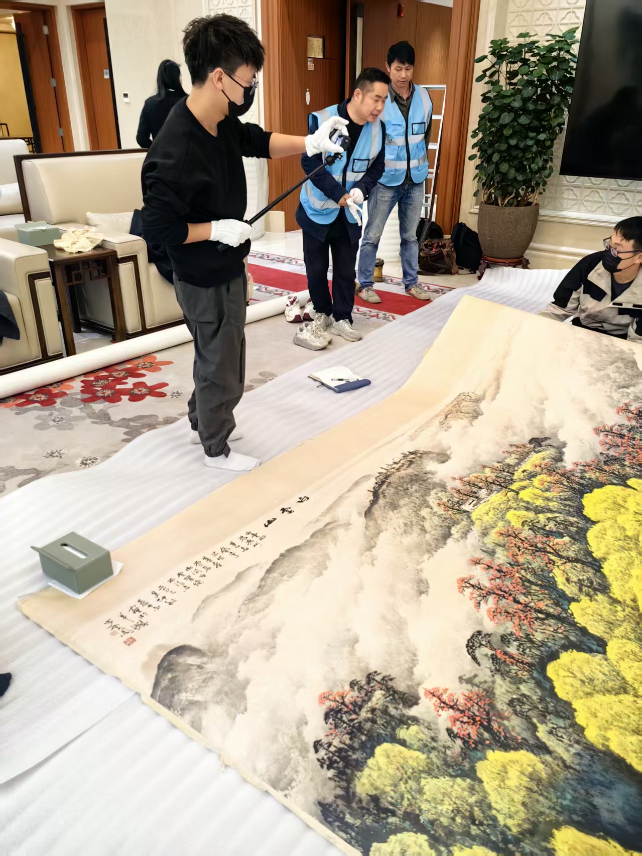 大幅卷轴平铺在专用缓冲毯上操作，避免弯折，多人协同平整转运